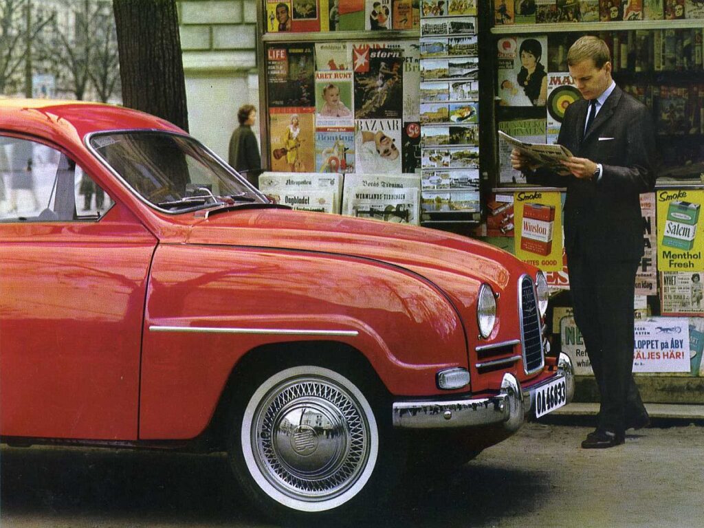 Roter Saab 96 Oldtimer vor einem Zeitungskiosk in einer Werbebroschüre von 1963. Ein Mann im Anzug liest davor Zeitung. Im Zeitschriftenregal im Hintergrund ist deutlich das Cover des US-MAD Magazins Ausgabe #71 (Juni 1962) mit der Zielscheibe zu erkennen.