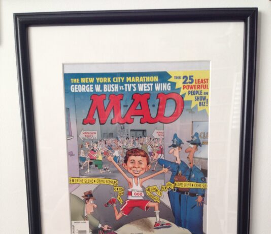 Gerahmtes, unveröffentlichtes Titelbild der US-Ausgabe MAD #411 von John Caldwell. Alfred E. Neuman rennt beim New York Marathon lachend durch ein Polizei-Absperrband an einem Tatort.