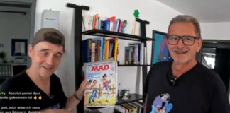 Paddy und der deutsche MAD-Zeichner Ivica Astalos stehen nebeneinander vor einem Regal. Paddy hält lächelnd ein klassisches MAD-Magazin in die Kamera.