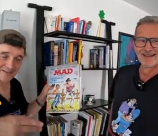 Paddy und der deutsche MAD-Zeichner Ivica Astalos stehen nebeneinander vor einem Regal. Paddy hält lächelnd ein klassisches MAD-Magazin in die Kamera.