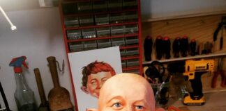 Abgeformter, noch haarloser Kopf der Alfred E. Neuman Büste während der realistischen Bemalung mit blauen Augen, Sommersprossen und Zahnlücke, davor eine Farbpalette.